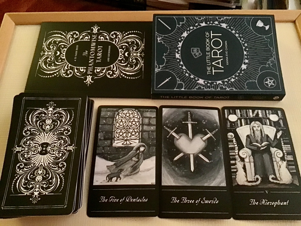 A tray with a mix of Tarot cards and books spread out on it. The cards have a black and white gothic style, and are the Phantomwise deck.